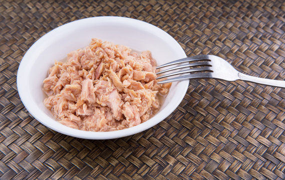 Pieces of canned tuna in a white bowl with a fork on wicker 