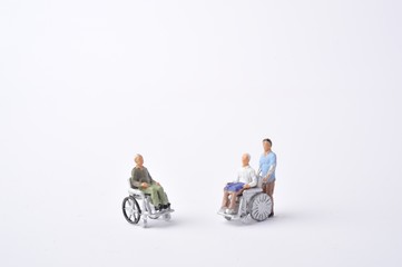 車椅子に乗っている高齢者と介助者のミニチュア人形