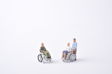 車椅子に乗っている高齢者と介助者のミニチュア人形