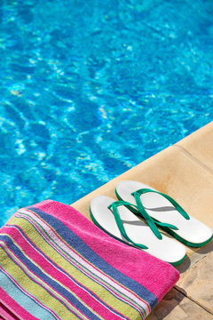 Pair of flip flop thongs and towel on the side of a swimming