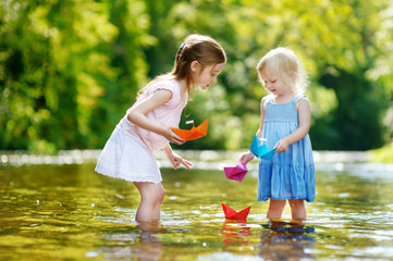Two little sisters playing with paper boats