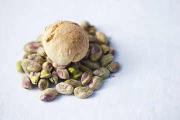 A handmade pistachio cookie on a pile of fresh pistachios on a white background.