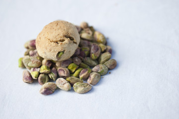 A handmade pistachio cookie on a pile of fresh pistachios on a white background.