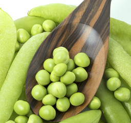 Fresh peas on wooden spoon with pods background