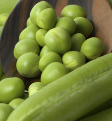 Fresh peas on wooden spoon with pods background