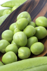 Fresh peas on wooden spoon with pods background