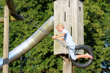 Happy school boy swinging  at playground sitting on old tire