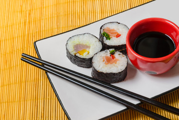 three sushi rolls with soy sauce and chopsticks