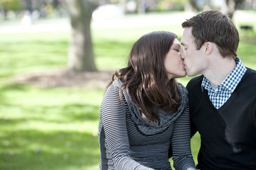 A romantic couple kissing on a sunny day in the park.