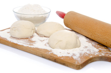 Three balls of pizza dough with a cup of flour and a rolling pin
