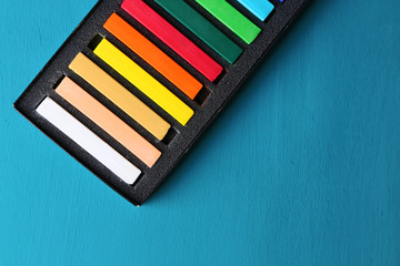 Colorful chalk pastels in box on color wooden background