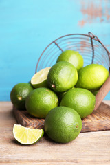 Fresh juicy limes in basket on blue wooden background