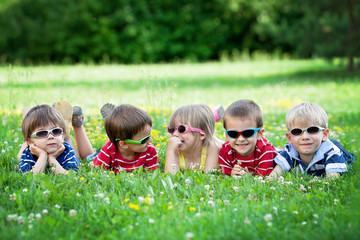 Five adorable kids, lying on the grass, smiling, having fun © Tomsickova