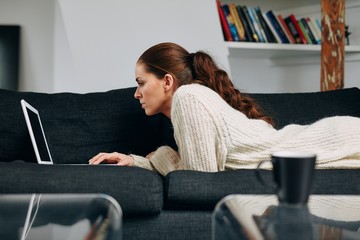 Relaxed young lady using laptop on sofa at home