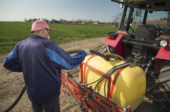 Farmer pouring water into tractor sprayer at field