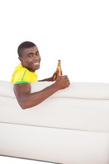 Happy brazilian football fan sitting on couch with a beer