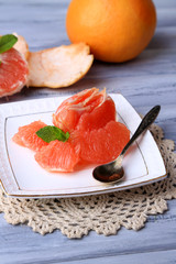 Ripe peeled grapefruits on plate, on color wooden background