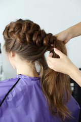 Naklejka premium Professional hairdresser braiding long brown hair of young woman in beauty salon, hair care and styling, intricate process of hair styling and care
