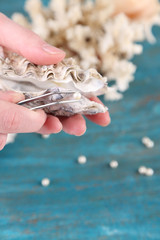 Hand with tweezers holding pearl and oyster on wooden