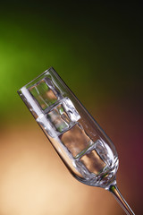 Glass with ice cubes on color background