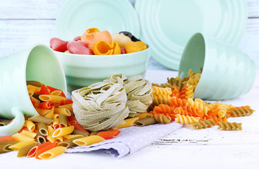 Colorful pasta in color bowls and mugs on wooden background