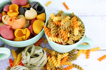Colorful pasta in color bowls and mugs on wooden background