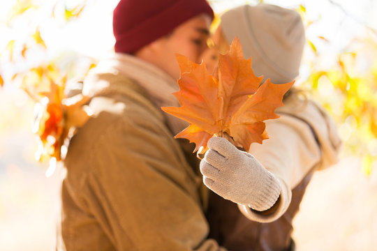 young couple kissing behind autumn leaves