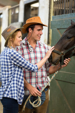 cowboy and cowgirl in stable touching a horse