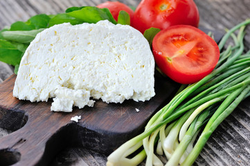 Cheese with tomatoes and arugula and onion on a wooden board