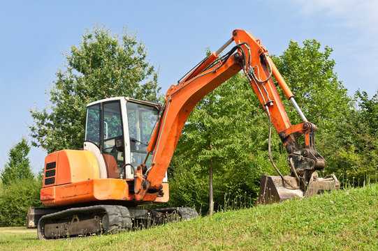 Ein Minibagger mit Raupenfahrwerk im Gr&uuml;nen unter blauem Himmel