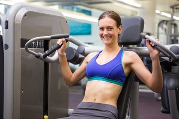 Fototapeta na wymiar Fit smiling brunette using weights machine for arms