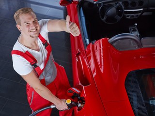 Car mechanic with fuel nozzle shows thumb up