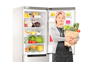 Woman with bag of vegetables in front of a fridge