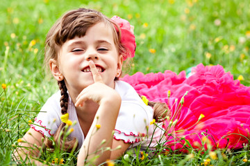 Happy child girl in a pink skirt covers her mouth with a finger