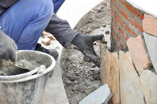 Mason worker installing flagstones on brick wall with mortar