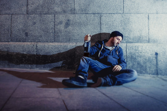 alcoholic drunk man sitting on street drinking alcohol bottle