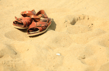 Fototapeta na wymiar Shoes. Brown leather sandals on a sandy beach. Summertime.