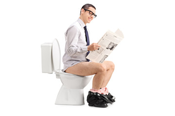 Man reading a newspaper seated on a toilet