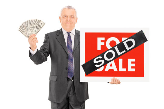 Mature businessman holding money and a sold sign