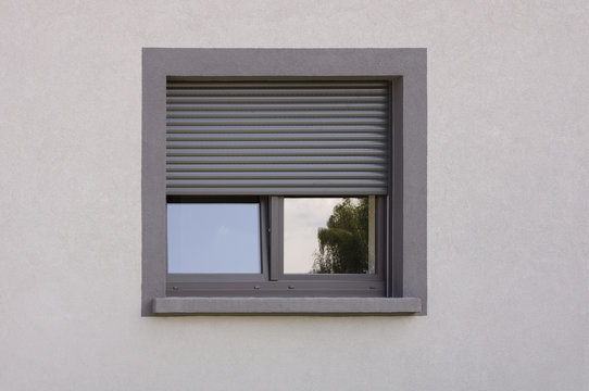 Dunkles Kunststofffenster mit Rollladen in grauer Fassade