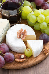 assorted soft cheeses and fresh grapes on wooden board, closeup