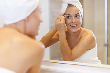 Woman tweezing eyebrows in front of mirror