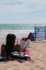 Chica tumbada en la playa leyendo