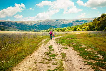 Fototapeta na wymiar Mother and daughter walk on road through field