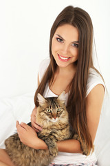 Beautiful young woman with cat sitting on bed