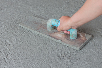 Close-up of hand using trowel to finish wet concrete floor