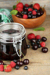 Tasty jam with berries in glass jar on wooden table