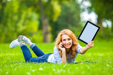Beautiful woman lying in grass with tablet