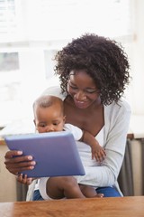 Happy mother holding baby son while using tablet pc