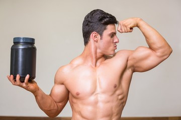 Naklejka na ściany i meble Muscular man posing with nutritional supplement in gym